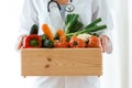 Nutritionist holding wooden box with fresh vegetables over white background.