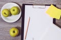 Close up of office accessorise: clipboard, a plate of apples, blank notepad on a wooden background. Weight loss starving dieting s