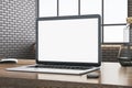 Close up of office desktop with empty white computer, supplies and other objects. Blurry brick wall and window with city view in Royalty Free Stock Photo