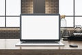 Close up of office workplace with empty white computer, supplies and other objects. Blurry brick wall and window with city view in Royalty Free Stock Photo