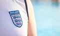Close-up of official England international football team logo on a sleeveless white shirt worn by a man