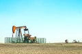 Close--up of oil well pump jack out in a field enclosed in a metal cattle fence with two other pumping wells in the distance all