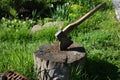 Close up of an old axe with a wooden handle stuck in a stump in the yard of a country house.