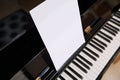 Close-up old black wooden piano with ivory and ebony piano keys and white paper sheet with copy space for notes