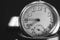 Close up of an An old clock face with numbers. Scratches on the glass. Silver chrome metal. Black background. Black and white