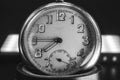 Close up of an An old clock face with numbers. Scratches on the glass. Silver chrome metal. Black background. Black and white