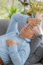 Close up of an old fat asian man with white hair wearing eye glasses and light blue shirt lying down on gray sofa alone in the Royalty Free Stock Photo
