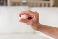 Close up of old female hand holding a red and white capsule pill in two fingers. Health care concept Royalty Free Stock Photo