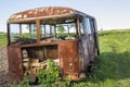 Close-up of old forsaken passenger bus with broken windows rusting in high green weedy grass on edge of plowed brown field on Royalty Free Stock Photo