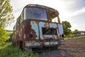 Close-up of old forsaken passenger bus with broken windows rusting in high green weedy grass on edge of plowed brown field on Royalty Free Stock Photo