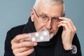 Close up old handsome man with gray hair and beard in eyeglasses and scarf thoughtfully looking on pills in hand over Royalty Free Stock Photo