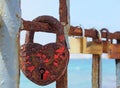 Close up of an old heart shaped red rusty padlock chained to a railing with others in a lone out of focus on a bright sunlit summe