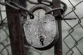 A close-up of an old locked iron lock with traces of paint on a thick chain wrapped between the gates of a metal fence on a gray