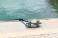 Close-up of old mooring bollard with a blue rope in the port against the background of the sea Royalty Free Stock Photo