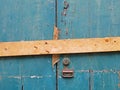 close up of an old peeling green painted wooden plank door barred shut with a piece of timber and rusty nails with a lock and Royalty Free Stock Photo