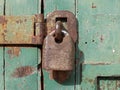 Close up of an old rusted metal padlock fastening an iron bar on a green wooden door Royalty Free Stock Photo