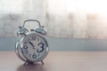 Close up old silver alarm clock on wooden table in bedroom with white curtain in the background. Royalty Free Stock Photo