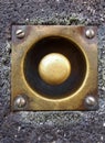 Close up of an old tarnished doorbell button with screws in a grey house wall