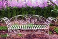 Old white iron bench in garden with colorful flowers purple orchids blooming on background