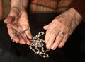 Close up of old woman praying with silver rosary with cross