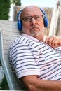 Closeup of a retired senior man looking to the side wearing blue headphones sitting on a lawn chair Royalty Free Stock Photo