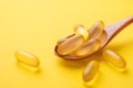 Close up Omega 3 capsules in wooden spoon on yellow background. Fish oil softgels. Supplement food vitamin D capsules