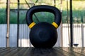 A close-up on one black sixteen kilogram weight with yellow stripes on the rubber floor in the gym with exercise equipment in