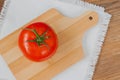 Close-up of one fresh red ripe tomato with water drops on branch, wooden background with rustic chopping board in center Royalty Free Stock Photo