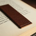 A close-up of an open book with a brown leather bookmark resting on the page. The Royalty Free Stock Photo