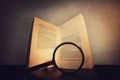 Close up of a open book on the table and a magnifying glass searching through the pages text. Old textbook sheets isolated on dark Royalty Free Stock Photo