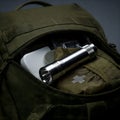 A close-up of an open dark green backpack revealing a silver flashlight, a white object, and a first aid kit inside. Generative AI Royalty Free Stock Photo