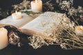 Close up of open vintage poetry book decorated with dried baby`s breath flowers. Blurred background with white lit burning candles