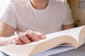 Close-up of opened thick paper book in hands of woman in white T-shirt