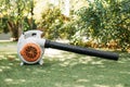 A close-up of an orange cordless, electric leaf blower lying on a grass. Autumn, fall gardening works in a backyard, on a lawn.
