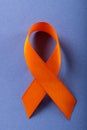 Close-up of orange leukemia awareness ribbon isolated against blue background, copy space