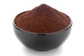 Close-Up of organic dark brown coffee granules in black ceramic bowl over white background