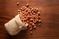 Close-up of organic red-brown peanuts Arachis hypogaea spilled out from a laying jute bag over wooden brown background