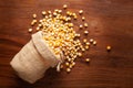 Close-up of organic yellow corn seed or maize Zea mays spilled out from a laying jute bag over wooden brown background