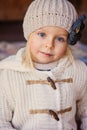 Close up outdoor portrait of adorable smiling child girl in beige knitted hat and coat