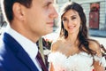 Close-up outdoor portrait of the young brunette bride with lovely sight and pretty smile looking in camera standing