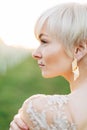 Close up outdoor profile portrait of beautiful woman with blond hair in elegant wedding dress and luxury earring posing Royalty Free Stock Photo