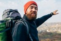 Close up outdoors portrait of young man indicate to the horizon in mountains with travel backpack and red hat. Royalty Free Stock Photo