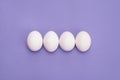 Close up overhead top view photo of four eggs in row with white shell isolated violet color background
