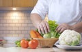 Overweight woman hand preparing various organic vegetables into bamboo basket for cooking on kitchen table Royalty Free Stock Photo