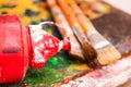Close up of paint brushes with a red plastic color over a color palette in a studio, in a blurred background
