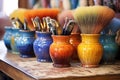 close-up of paintbrushes and colorful glazes on pottery table