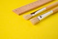 Close-up of paintbrushes next to a wooden ruler on a bright yellow background