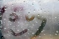 Close-up of a painted smiling smiley face on a window with raindrops in the daytime. The concept of a happy mood in bad weather