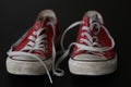 Close up of pair of sneakers - red and white vintage worn out shoes - youth hipster shoes on black background Royalty Free Stock Photo