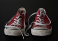 Close up of pair of sneakers - red and white vintage worn out shoes - youth hipster shoes on black background - top view Royalty Free Stock Photo